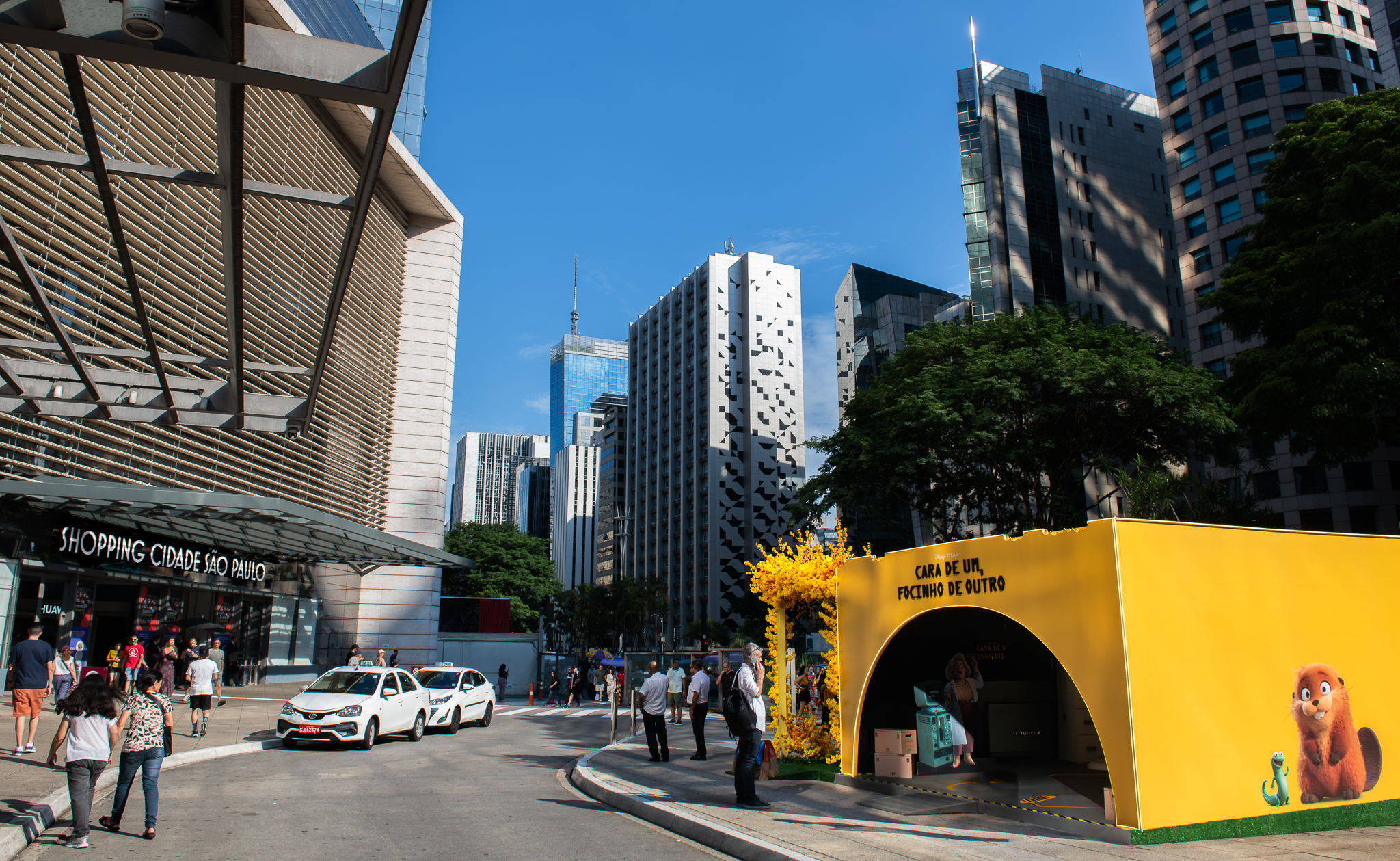 Stand de ativação de marca amarelo com personagens animados na Avenida Paulista, São Paulo, em frente ao Shopping Cidade São Paulo