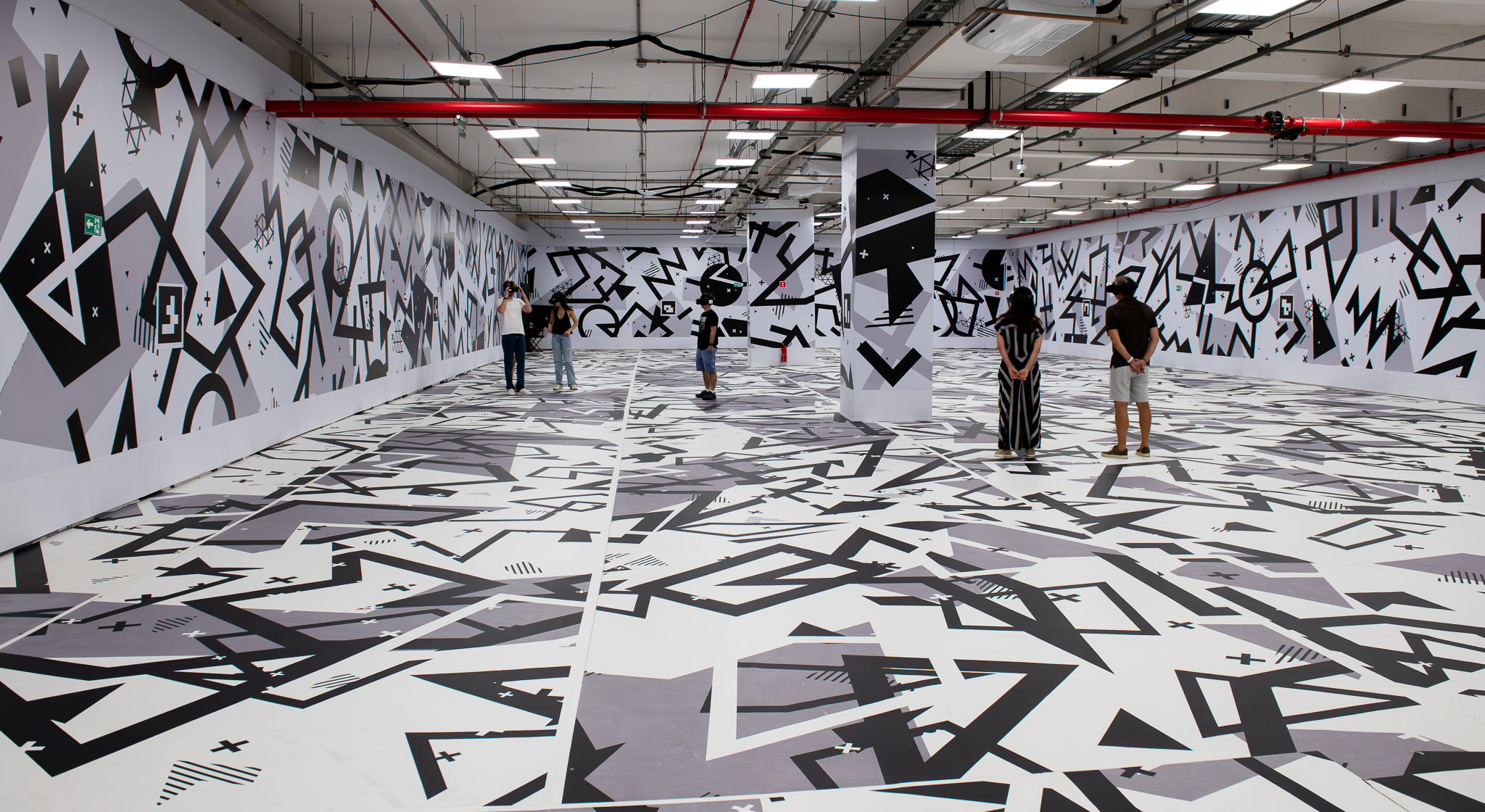 Instalação artística imersiva em preto e branco com grafismos geométricos cobrindo piso e paredes de estacionamento de shopping center em São Paulo