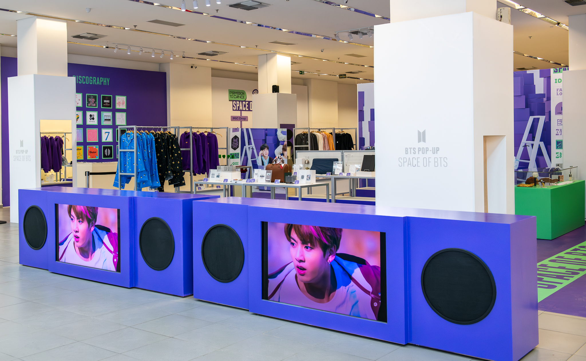 Loja pop-up BTS Space of BTS em shopping center com painéis em roxo, telas com integrantes do grupo e produtos oficiais à venda