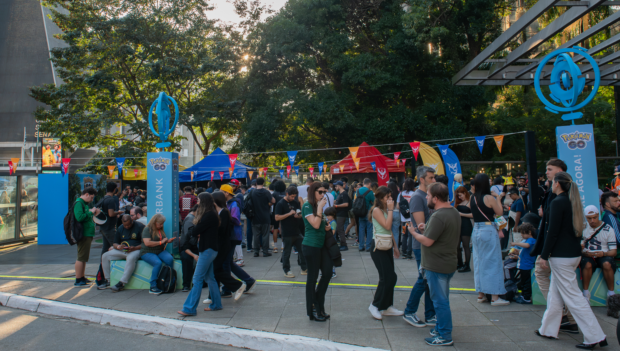 Evento Pokémon GO com grande público em área externa de shopping center em São Paulo com decoração temática das equipes e Pokéstops