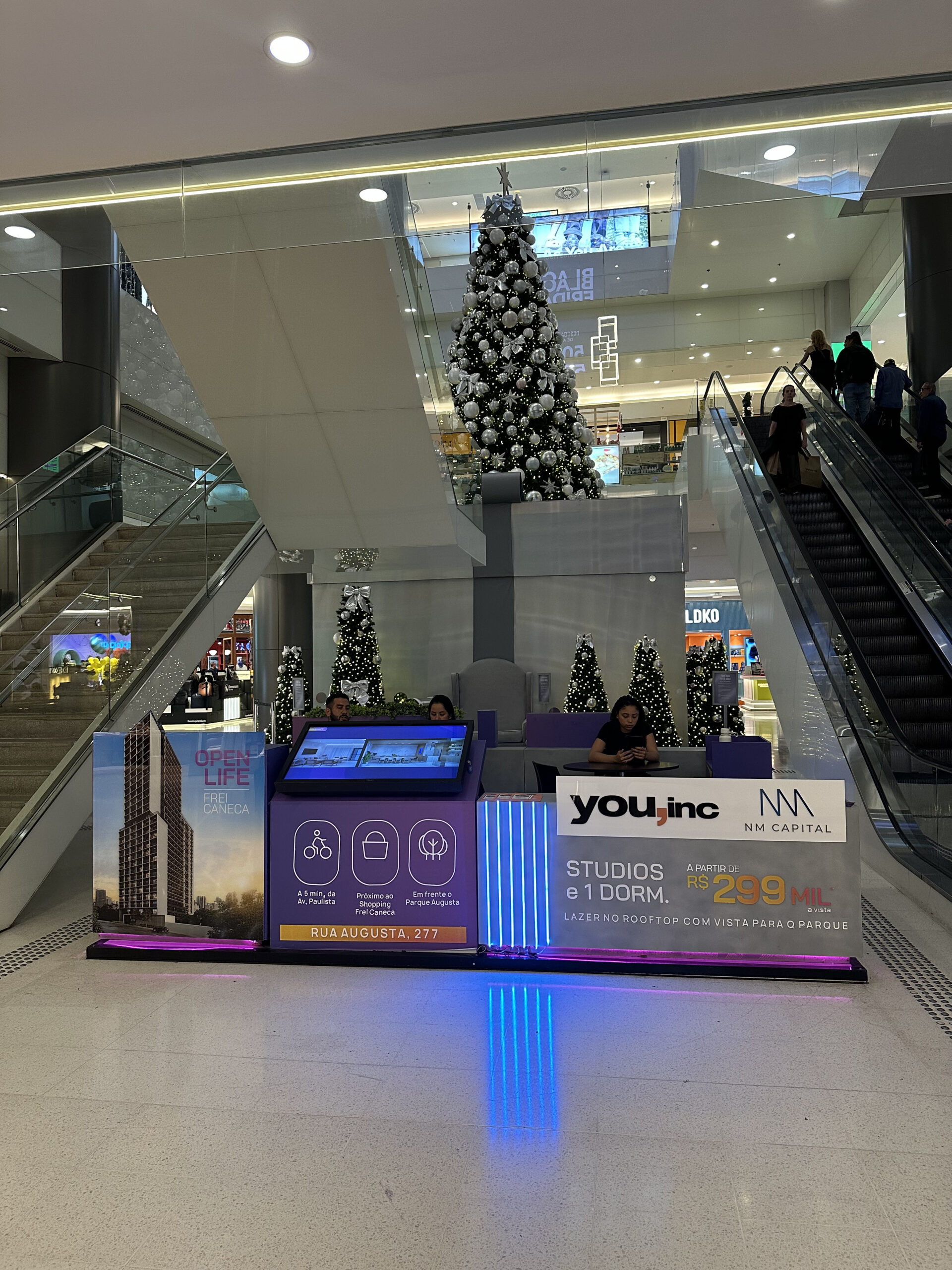 Stand imobiliário You.inc NM Capital no Shopping Frei Caneca com totem iluminado e decoração natalina ao fundo
